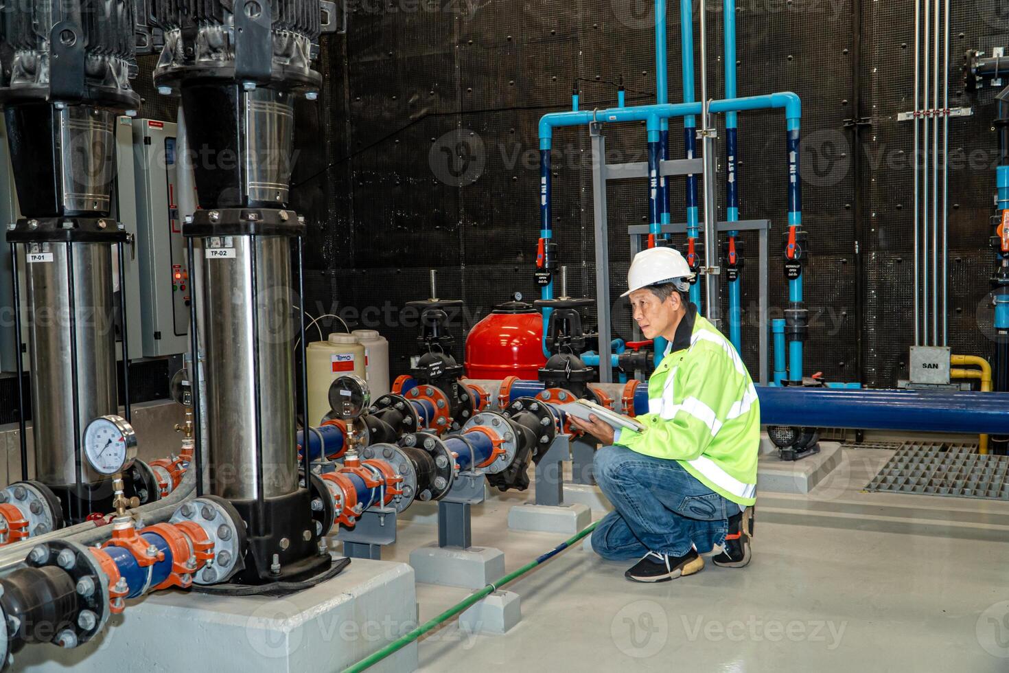 asian man worker in protective uniform and with hardhat using tablet for checking temperature in pipes Factory interior. photo