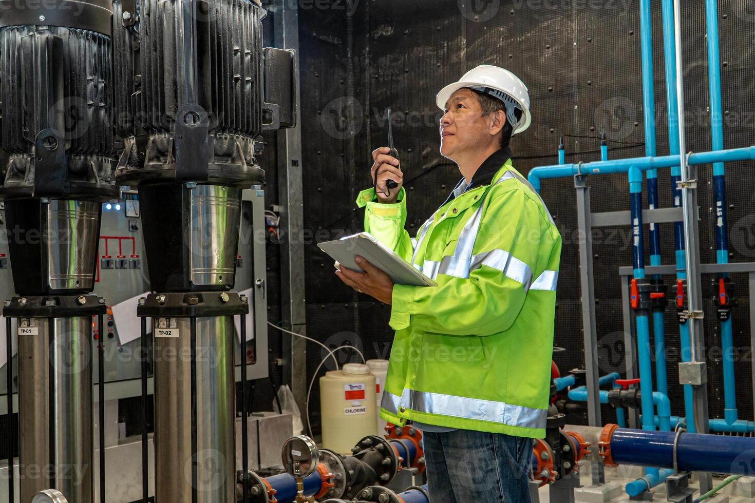 asian man worker in protective uniform and with hardhat using tablet for checking temperature in pipes Factory interior. photo