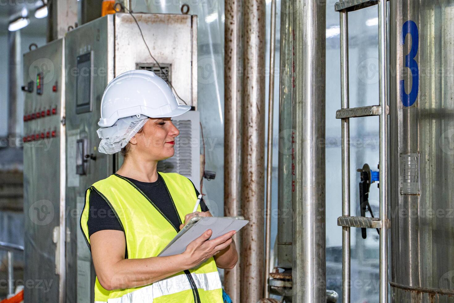 Female industrial engineer wearing a white helmet while standing in a heavy industrial factory photo