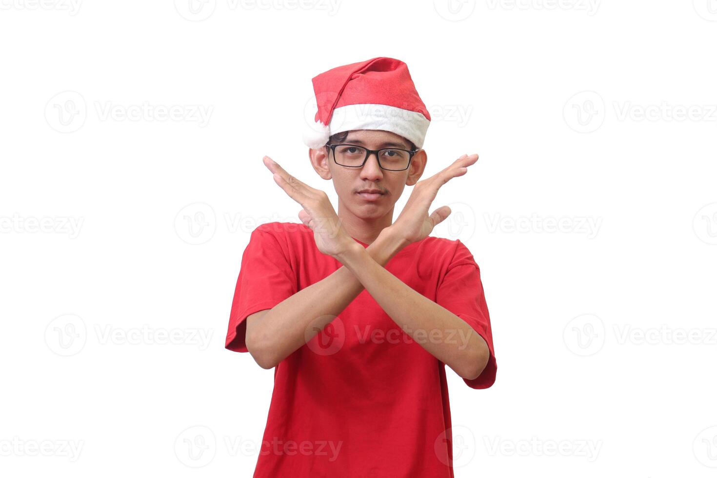 Portrait of excited Asian man in red t-shirt with santa hat showing X sign of hands. Teenager refusing an invitation from someone. Isolated image on white background photo