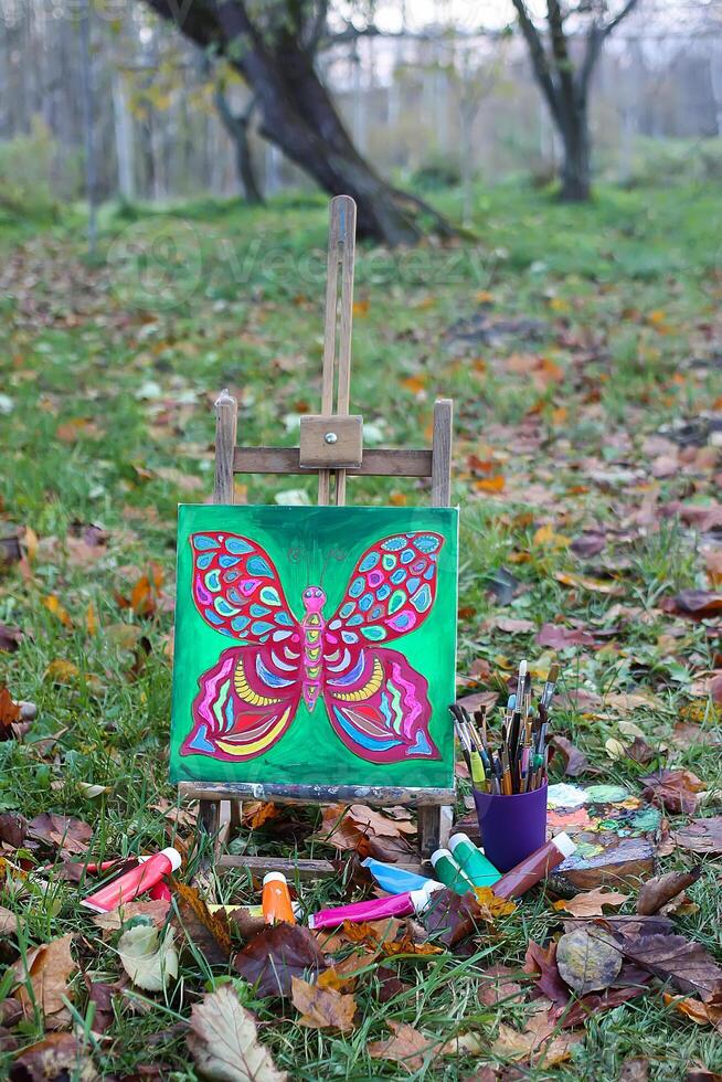 Easel with paints and painting on canvas in autumn park photo