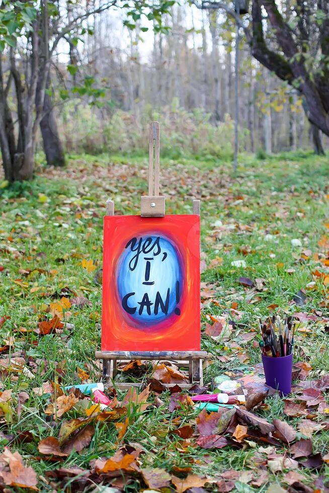 Easel with paints and painting on canvas in autumn park. photo