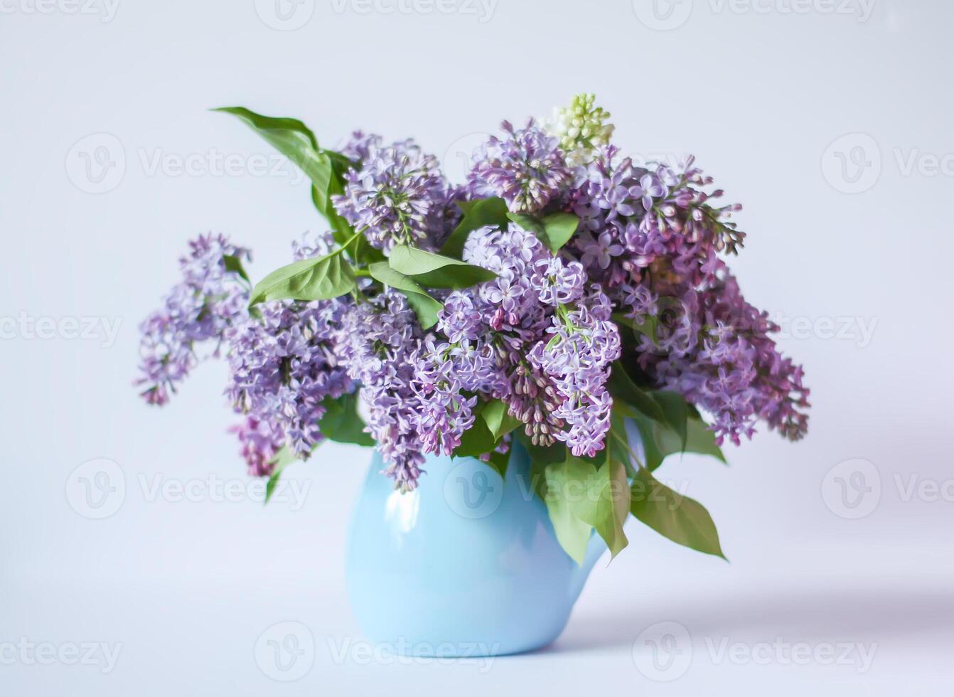 Beautiful bouquet of fragrant purple flowers in blue ceramics vase on light background. Syringa vulgaris or lilacs plant. photo