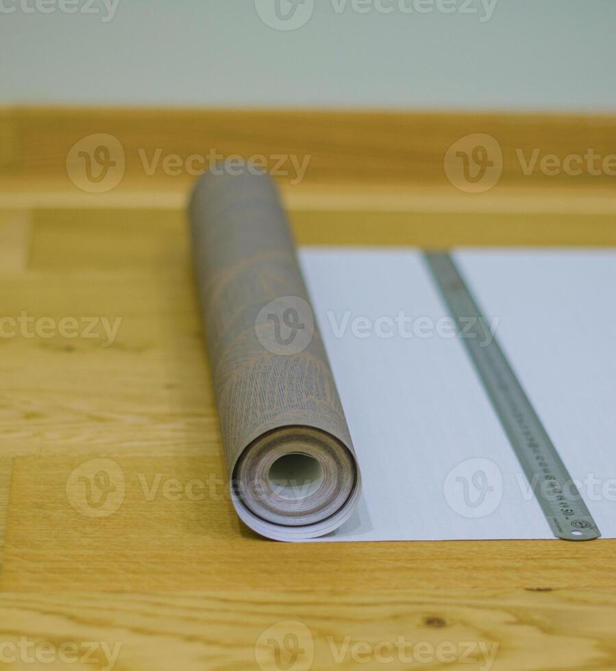 roll of wallpaper lies on wooden floor with metal ruler . High quality photo