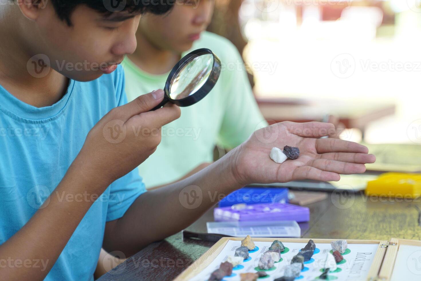 Asian boys study the composition of different types of rocks with a magnifying glass. Concept of learning outside the classroom, science, geology. photo