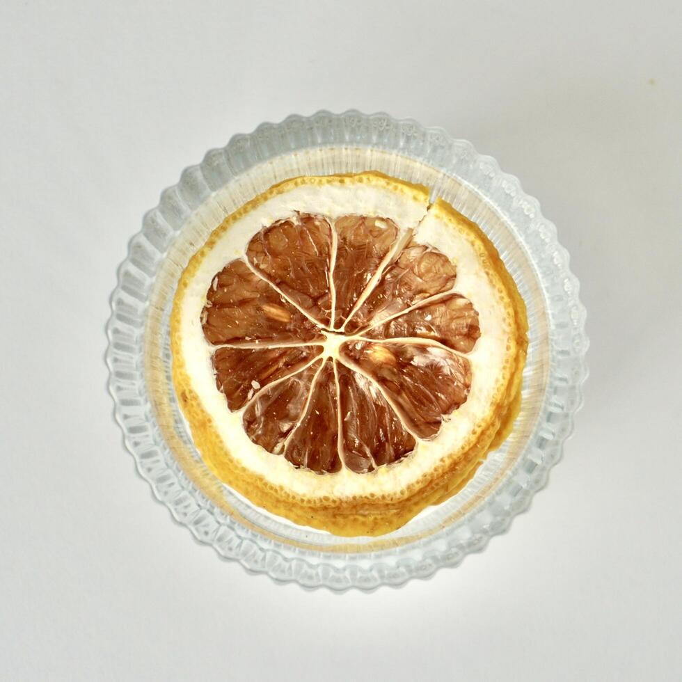 Dry lemon slices inside round glass bowl container isolated on square white background from above shot angle view. photo
