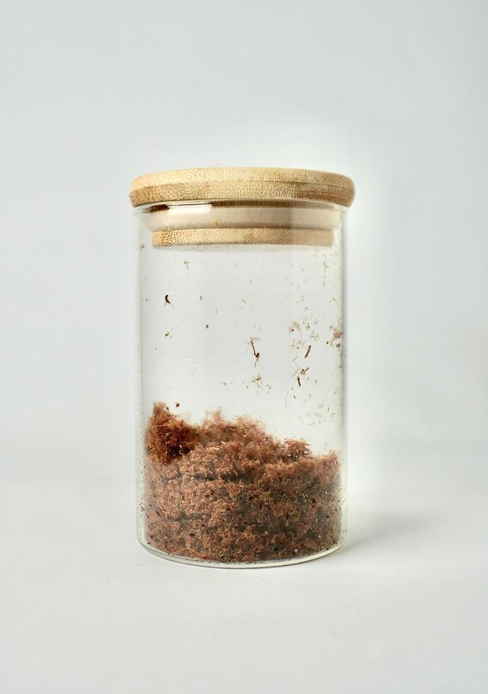 Beef meat floss or abon sapi in round transparent glass jar container isolated on vertical white background. photo