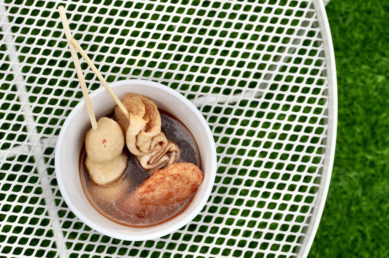 Oden fish cake food sticks with soup isolated on horizontal white table and green grass floor background from above top angle view. photo