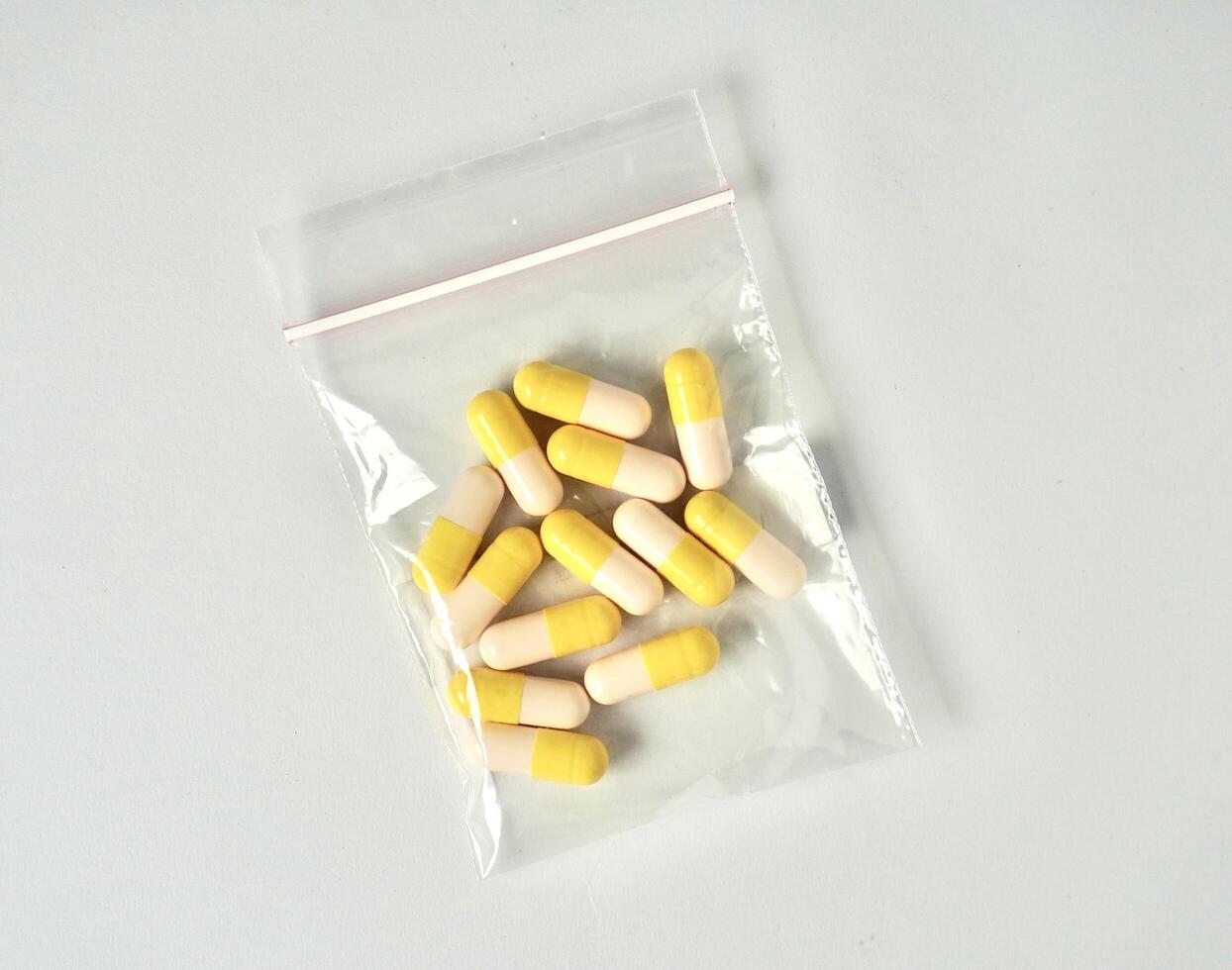 Groups of white and yellow colored cough and flu medicine capsules in plastic bag. Healthcare object photography isolated on horizontal white background. photo