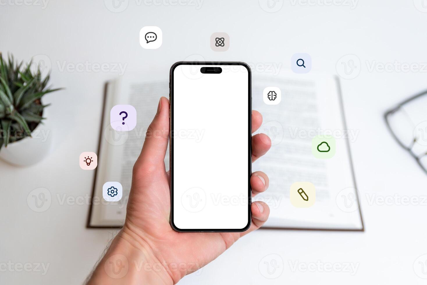 Phone mockup in hand in front of open book with flying icons, question mark, idea, cloud, pen, atom, brain. Great for learning, tech, education visuals photo