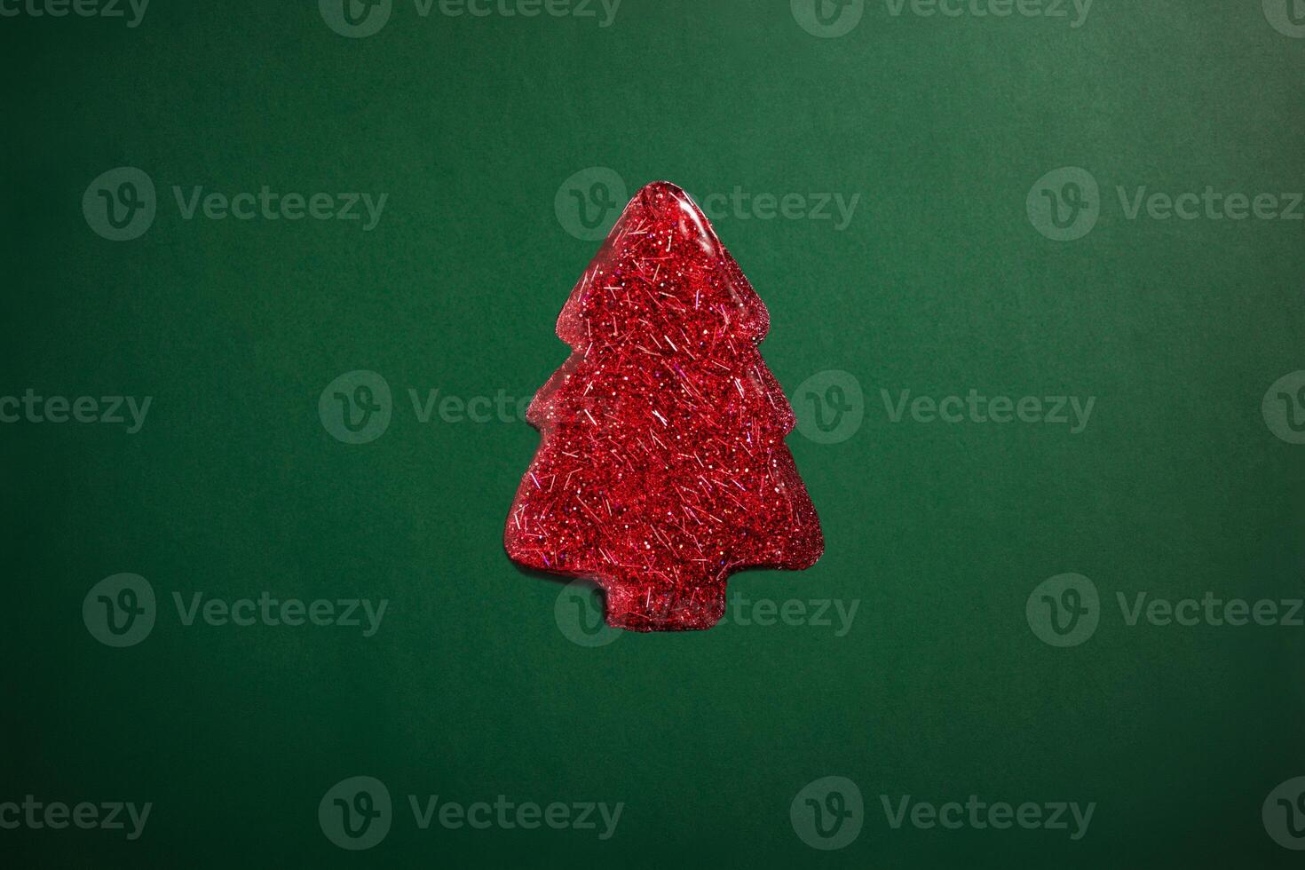 red sparkly jelly shaped like a Christmas tree on green background. Minimalistic holiday photo