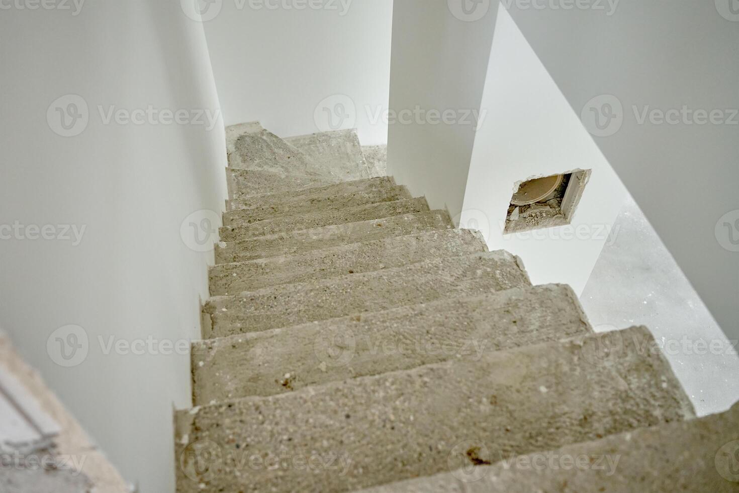 Empty apartment with unfinished concrete staircase and white walls undergoing renovation. Interior of building under construction photo