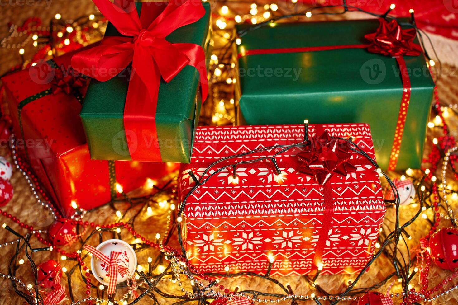 Wrapped Christmas gifts in red and green with bows and ribbons surrounded by glowing garland lights and festive ornaments photo