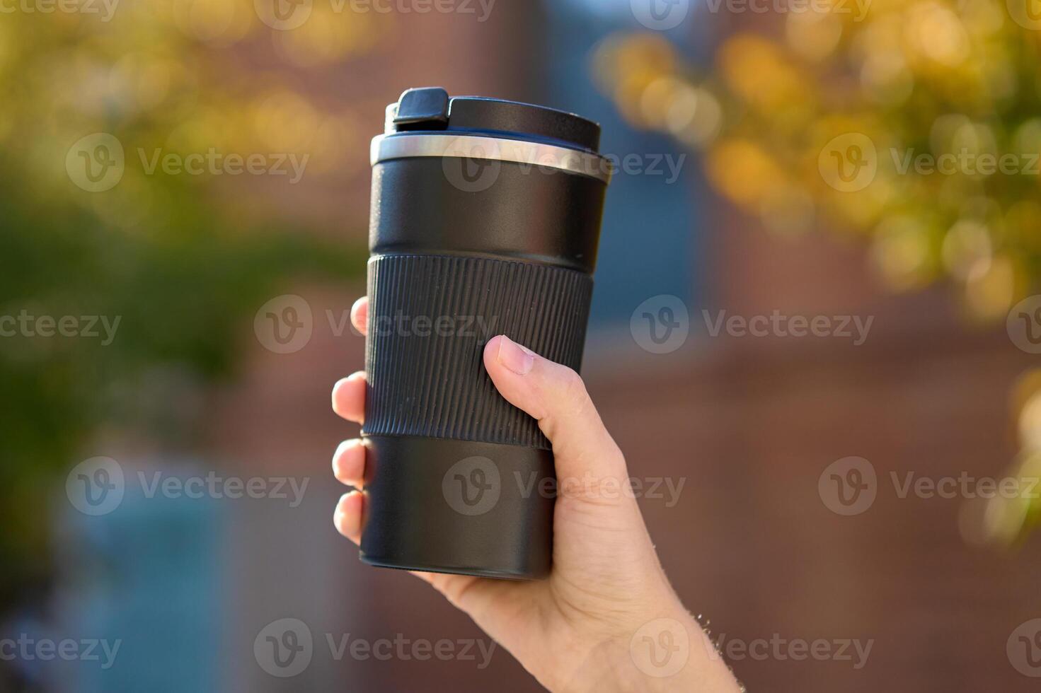 Woman holding reusable coffee cup on blurred autumn background. Concept of sustainable and eco-friendly living photo
