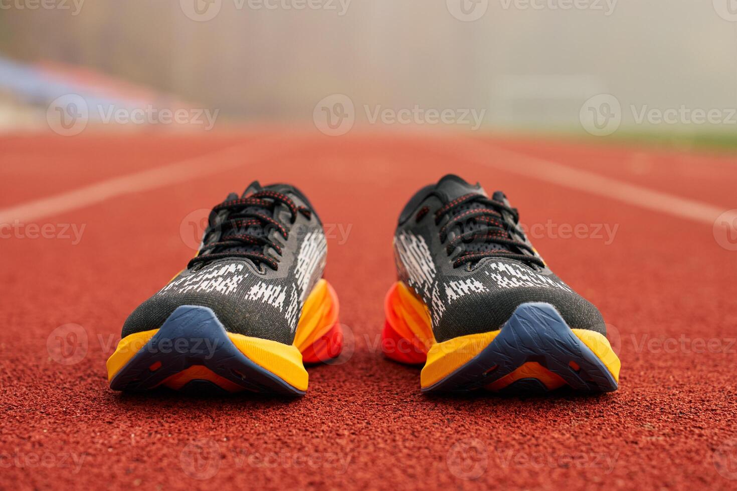 Pair of black and orange running shoes on red running track. Concept of sports training in outdoor setting photo