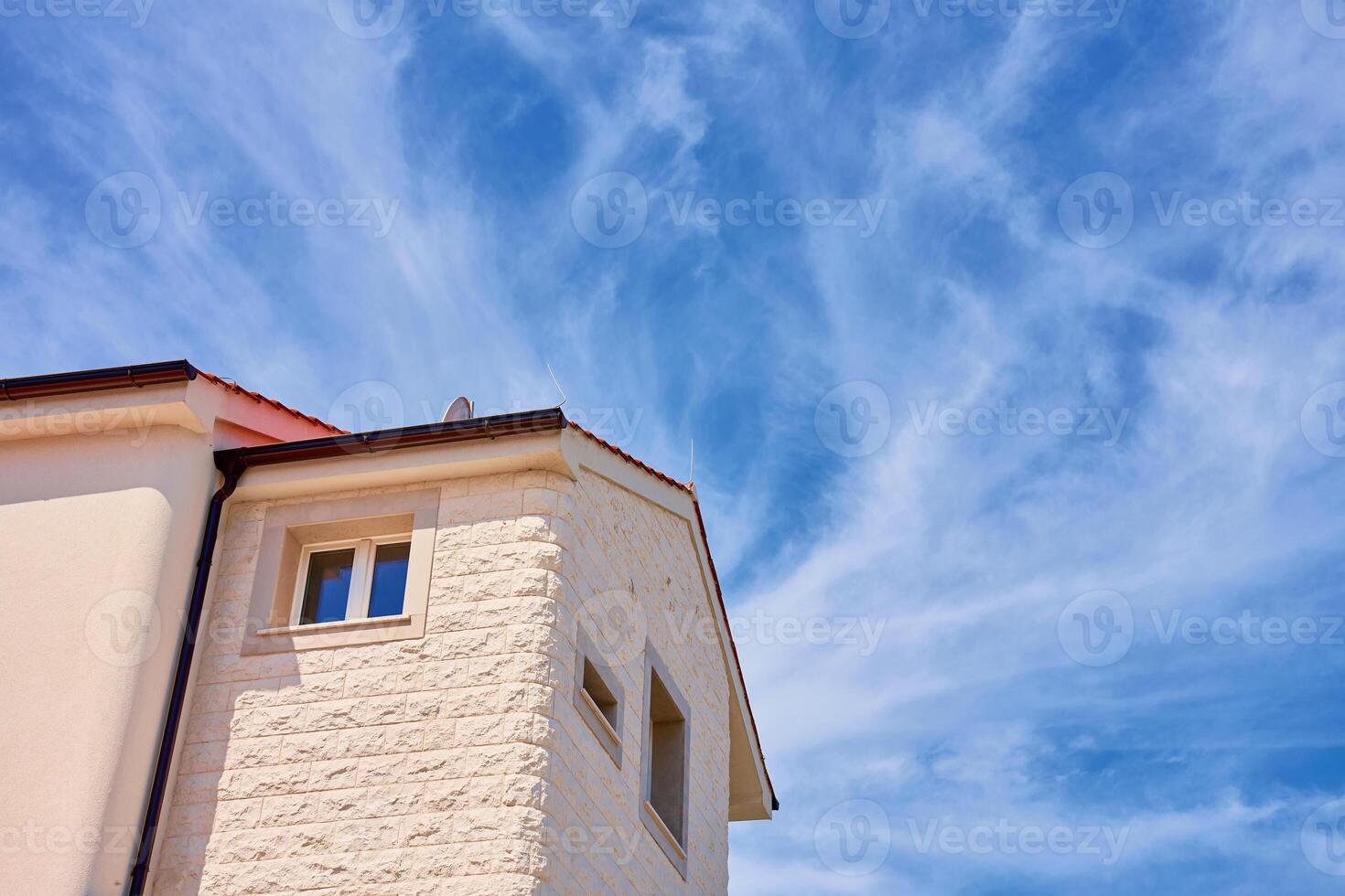 Modern Mediterranean house with red tile roof and white stone facade under bright blue sky. Typical architecture of residential building in coastal town photo