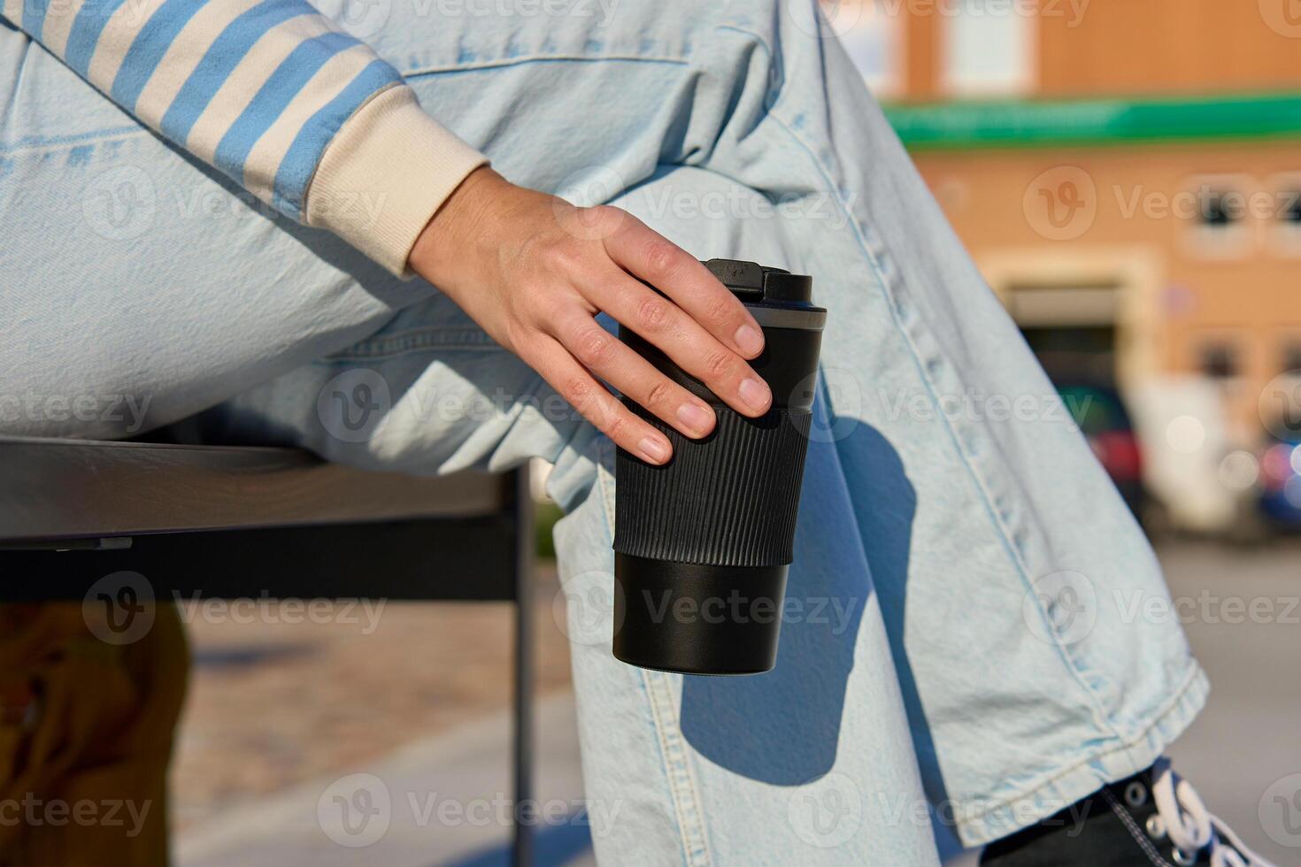 Woman in striped sweater and blue jeans enjoying her coffee break outdoors, holding black reusable coffee cup photo