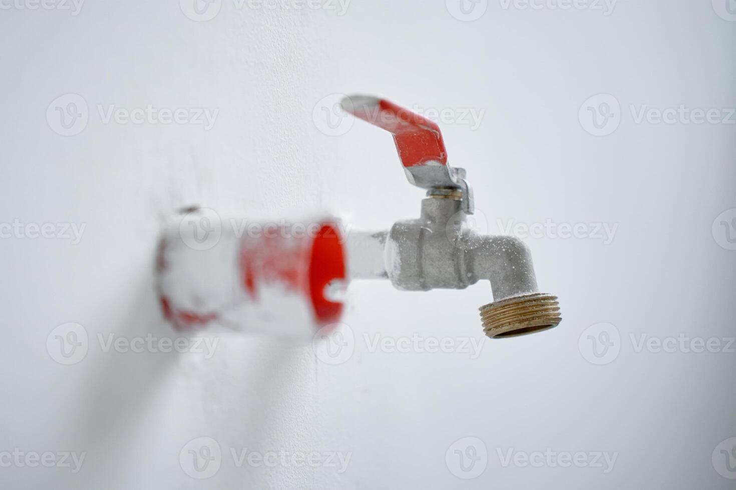 Close-up of water faucet with red handle protruding from white wall in empty apartment. Plumbing work during home renovation photo
