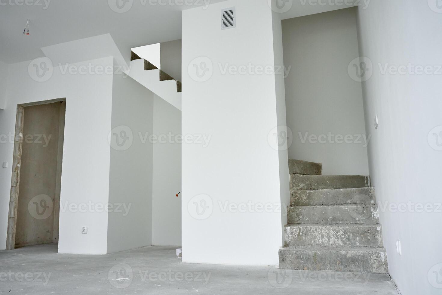 Empty apartment with unfinished concrete staircase and white walls undergoing renovation. Interior of building under construction photo