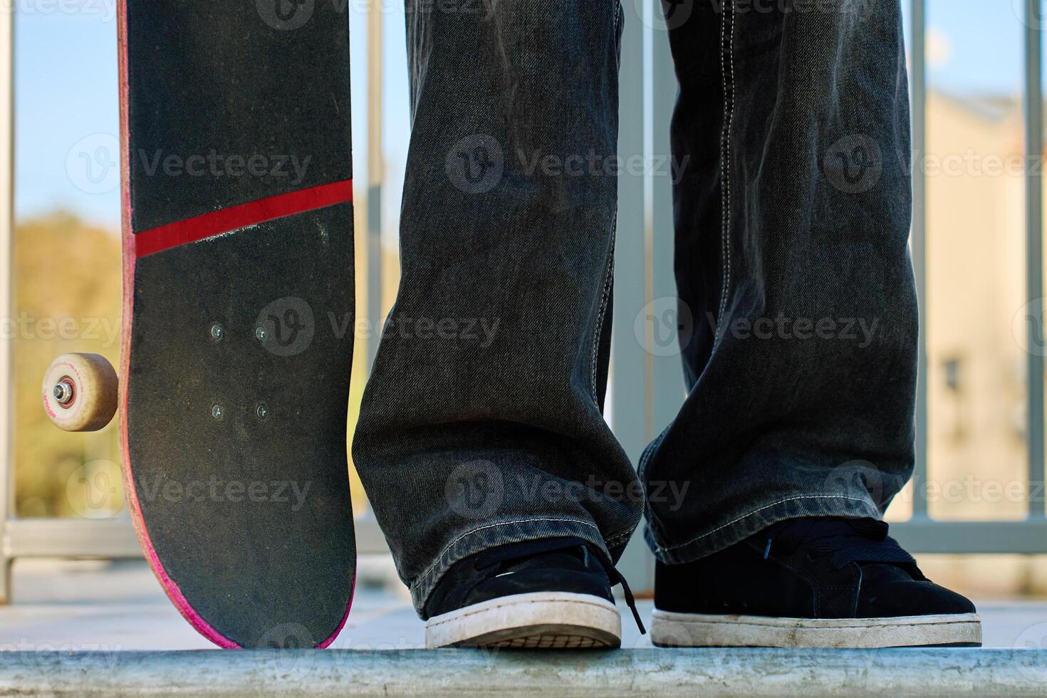 Skateboarder in baggy jeans holding scratched pink skateboard at city street. Teenager is skateboarding. Concept of youth subculture photo