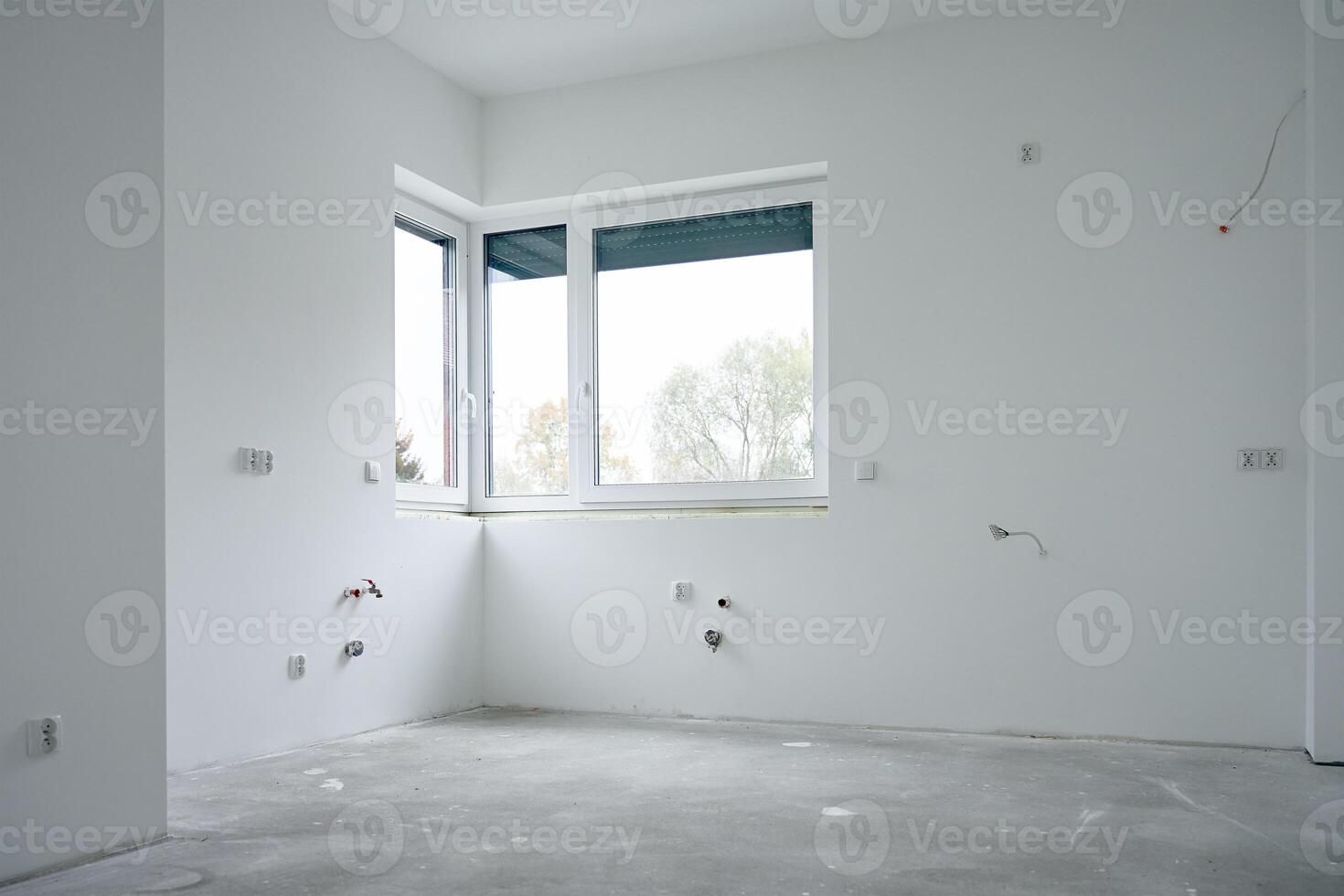 Spacious empty apartment undergoing renovation with large window, concrete floor and white walls. New building under construction photo