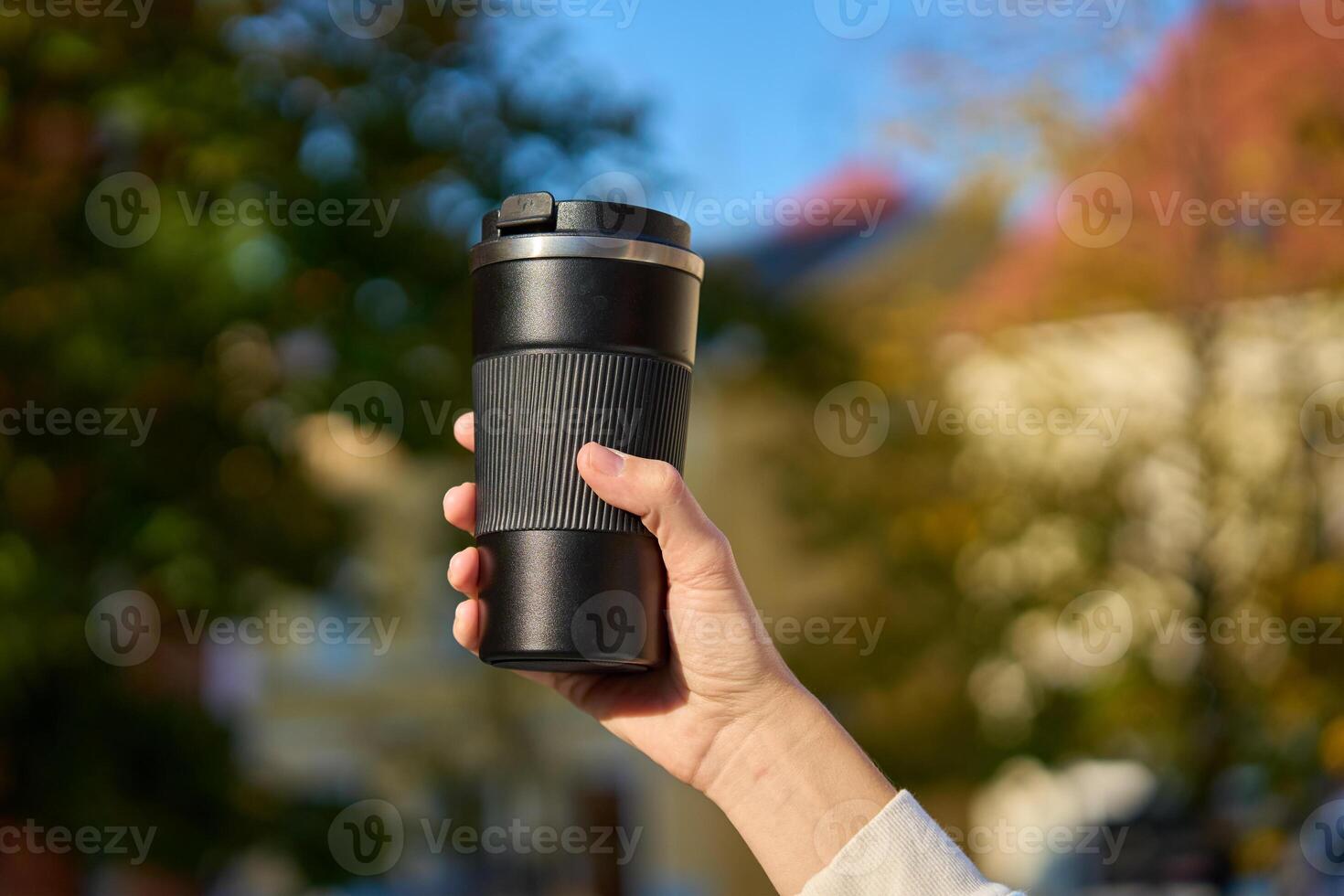 Woman holding reusable coffee cup on blurred autumn background. Concept of sustainable and eco-friendly living photo