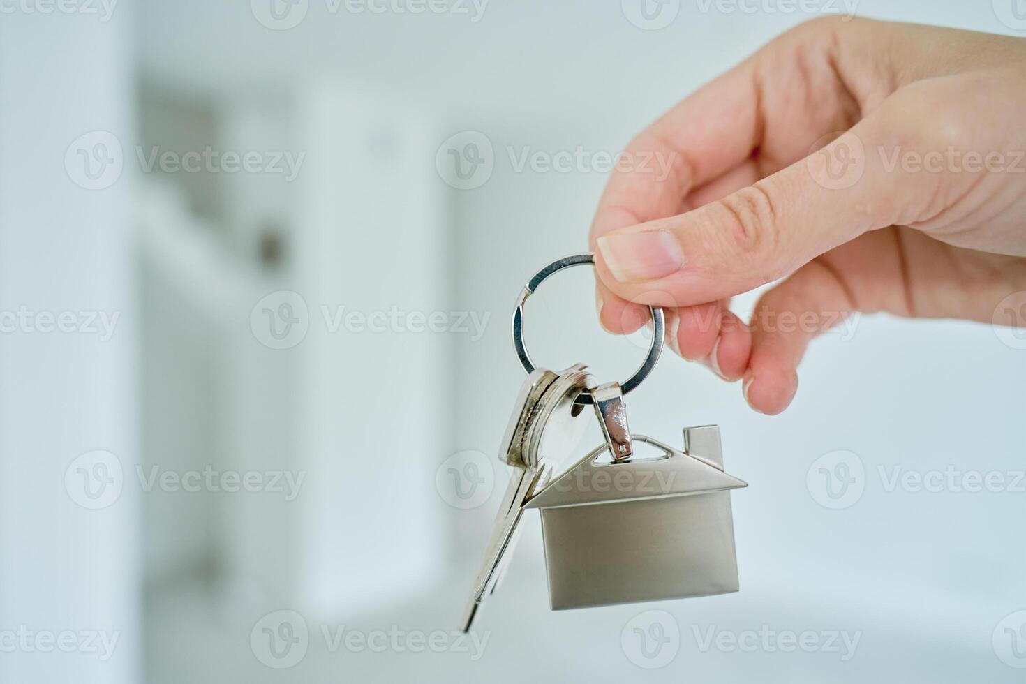Close up hand holding keys with house shaped keychain in front of blurred new apartment interior. Concept of mortgage and new house purchase. Real estate transactions photo