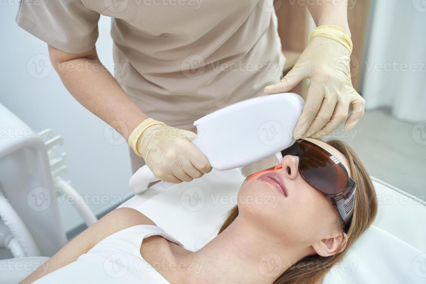Laser facial treatment for hair removal and rejuvenation at spa. White equipment enhances beauty and skin care. The cosmetologist uses advanced technology for therapy, promoting health, cosmetic care photo