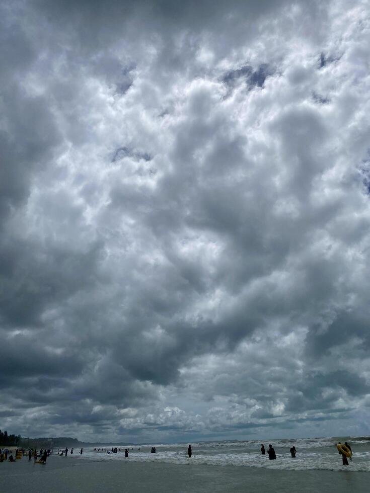 A cloudy sky over the ocean with people walking on the beach photo