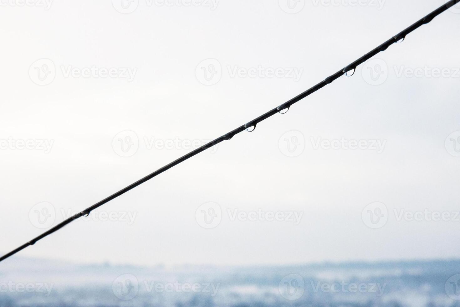 Minimalistic closeup of vineyard wire with delicate water droplets against cloudy overcast sky. Rain drops against a blurred horizon. Copy space photo