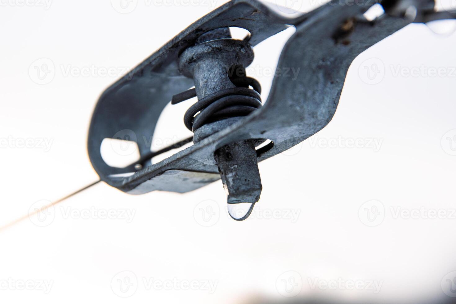 Closeup of metal vineyard wire tensioner with water droplet in cold winter setting. Metal construction component, industrial design and durability amidst a winter vineyard landscape. Copy space photo