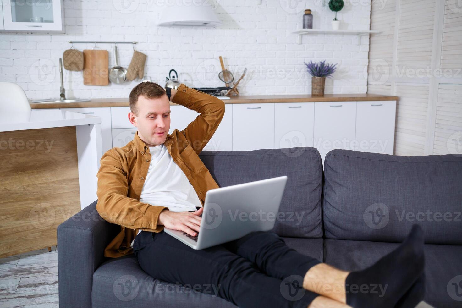A young successful man is sitting at home on the couch with a laptop and working. Remote work during quarantine. photo