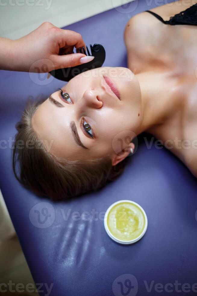 A young woman is lying on a couch and she is having a face massage, skin care, prevention of wrinkles on the face, skin improvement. Beauty procedures for women photo
