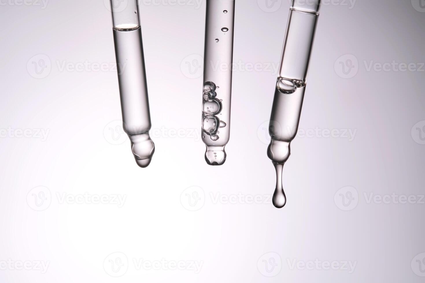 Three pipettes with a cosmetic product. Serum or fluid drips from one of them. photo