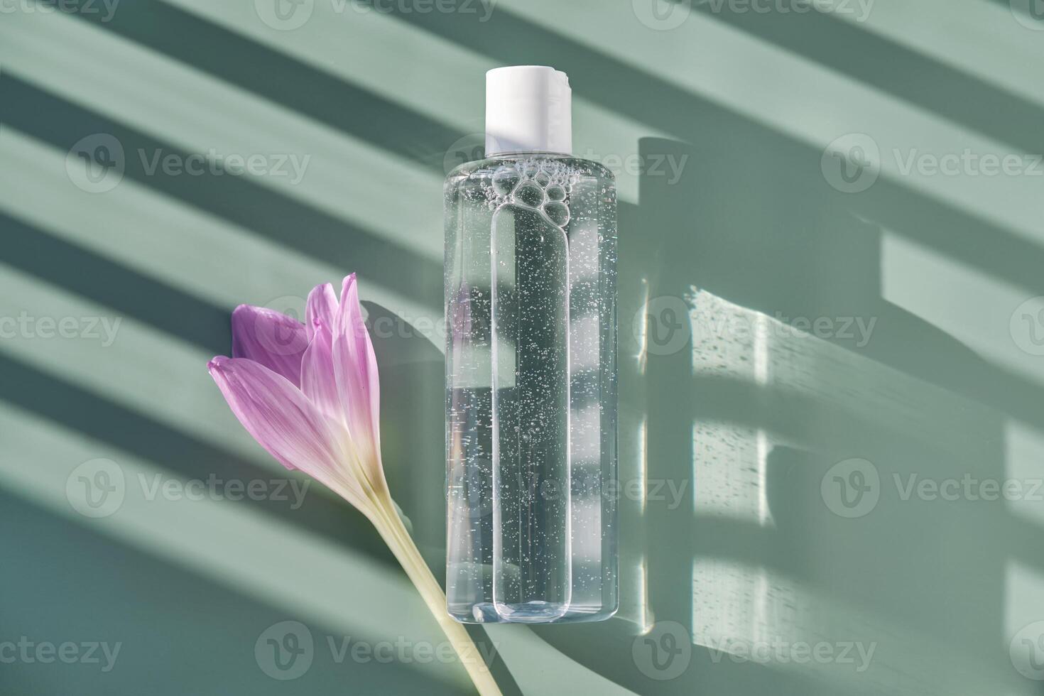 Bottle of facial toner or cleanser on a green background with stripes shadows. photo