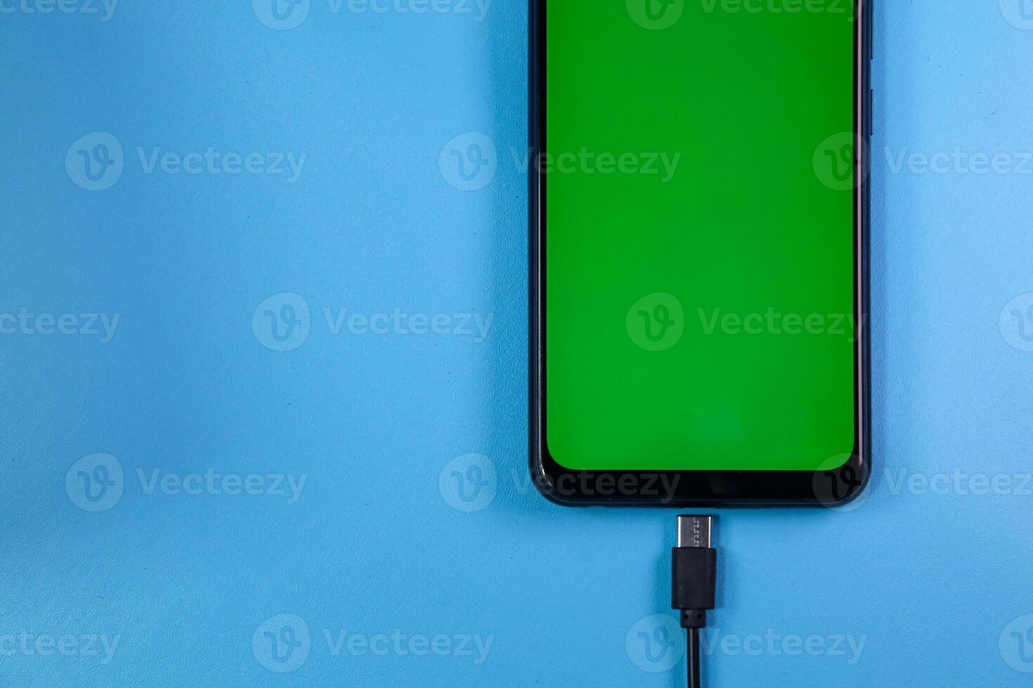 mobile phone with green screen connected to a charger on blue background photo