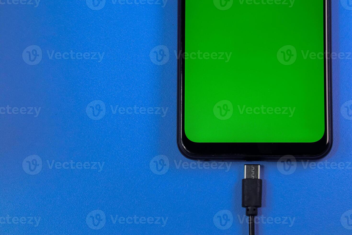 mobile phone with green screen connected to a charger on blue background photo