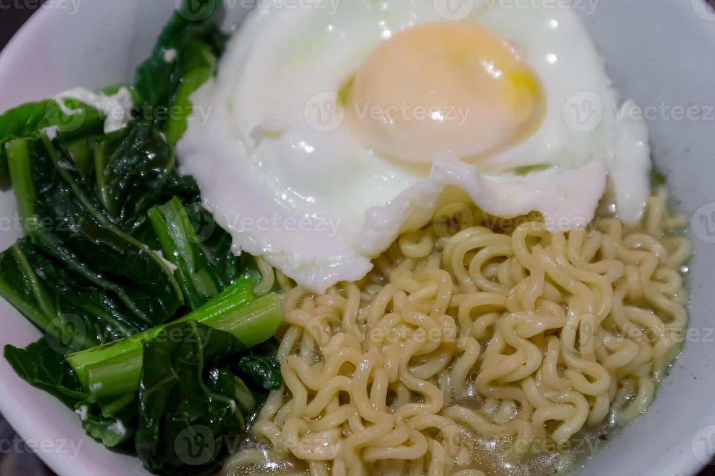 close up noodles in a bowl with sunny side up egg and vegetables photo