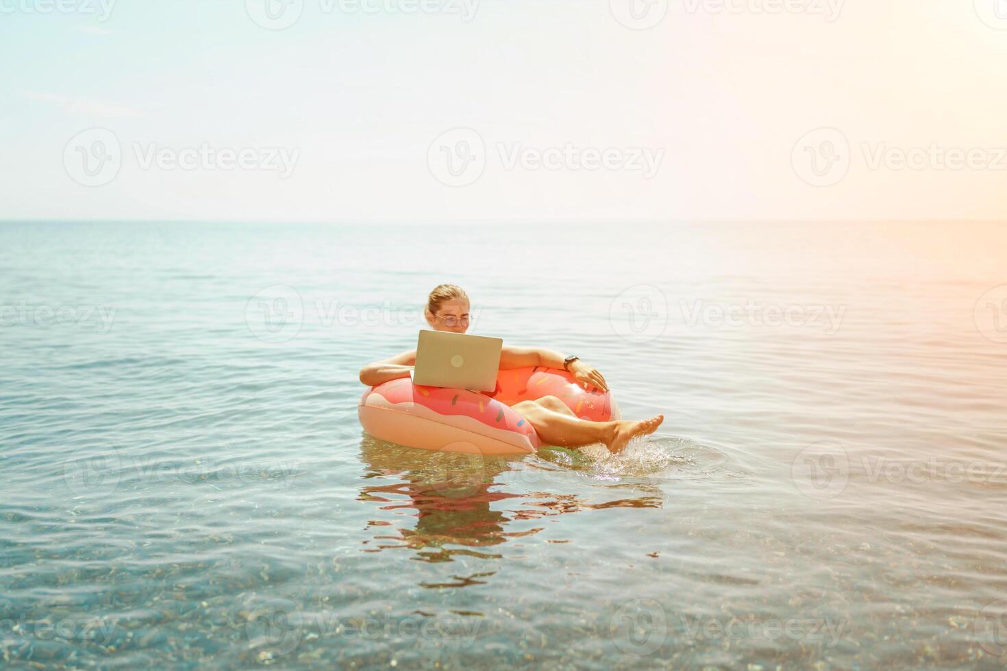 Woman laptop sea. Freelancer woman in sunglases floating on an inflatable big pink donut with a laptop in the sea. People summer vacation rest lifestyle concept photo