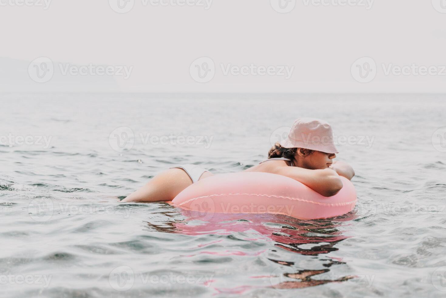 A woman is laying on a pink inflatable raft in the ocean. The scene is peaceful and relaxing, with the woman enjoying the water and the sun. photo