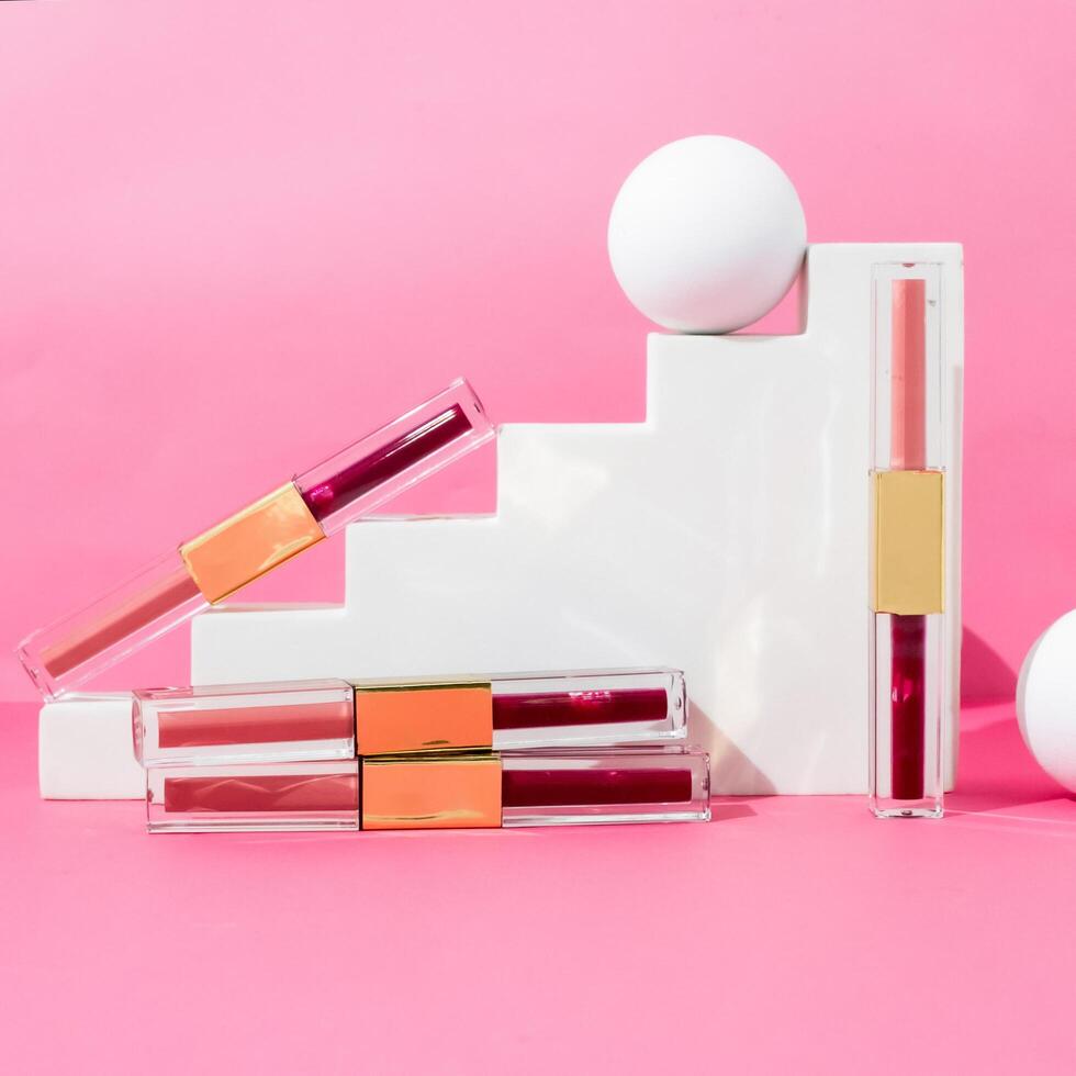 Lip glosses and a white ball on a pink background photo