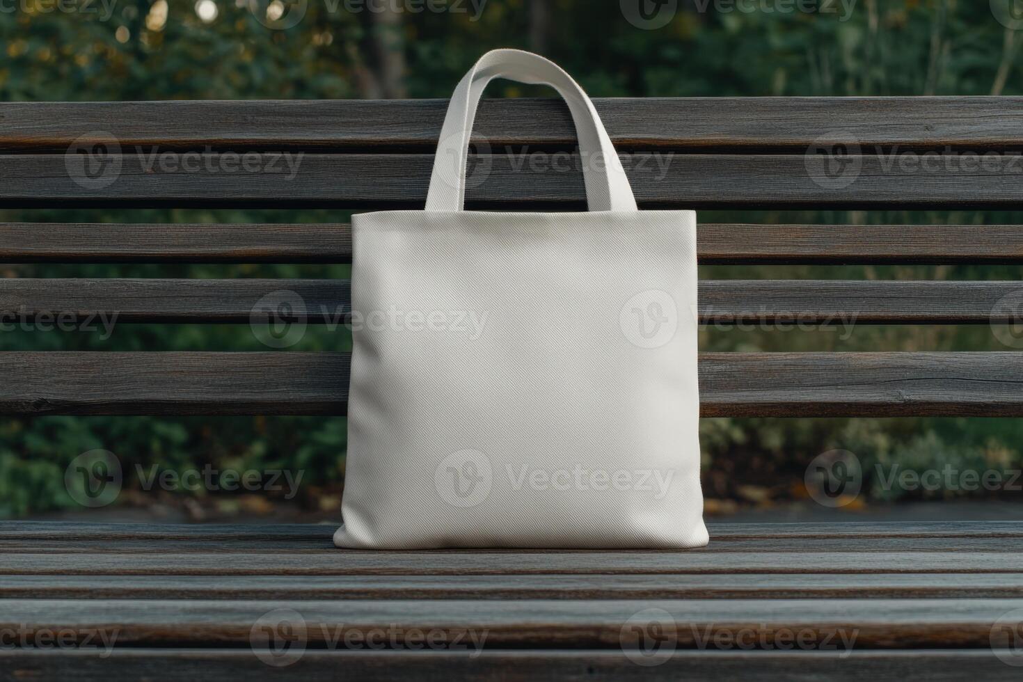 A simple white tote bag rests on a wooden bench in a park photo