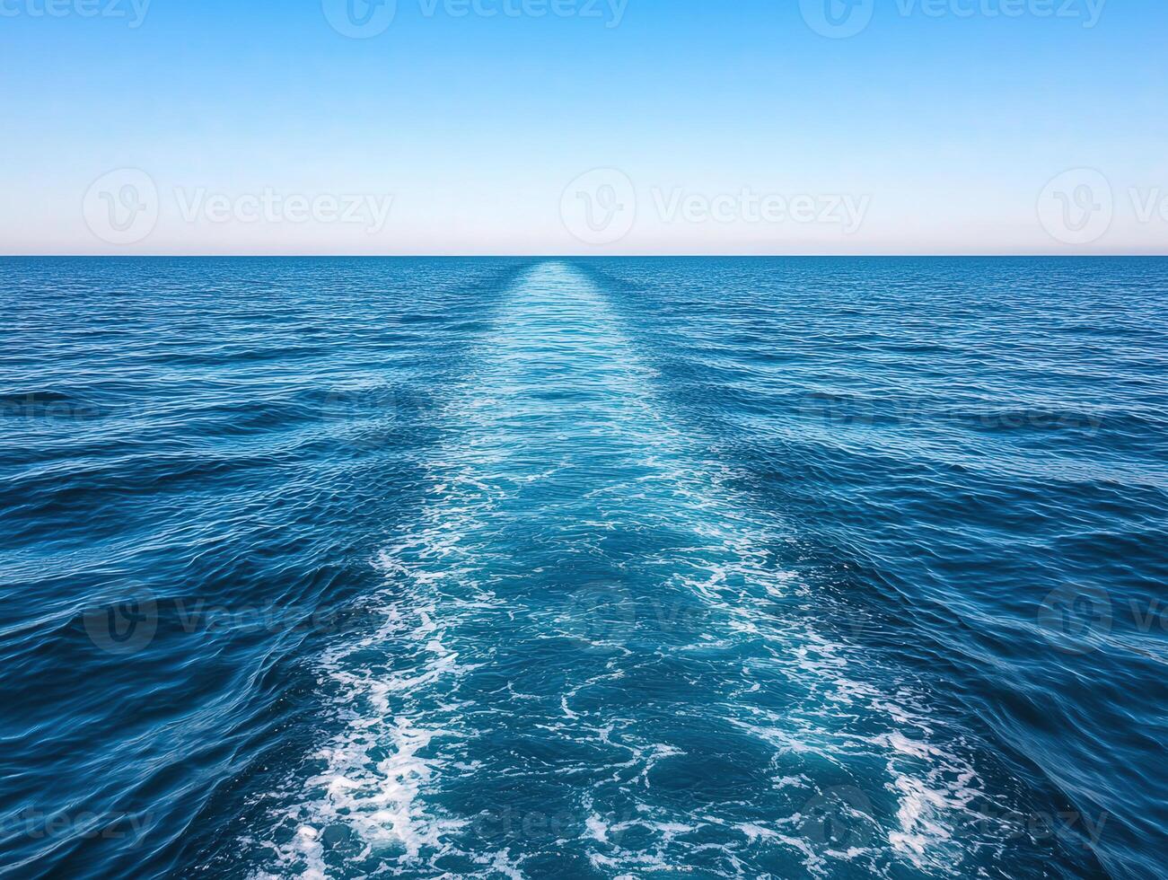 Calm blue ocean waves and wake trail from a boat on a sunny day photo