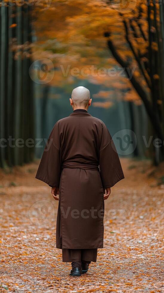 A monk walks through an autumn forest path surrounded by trees photo