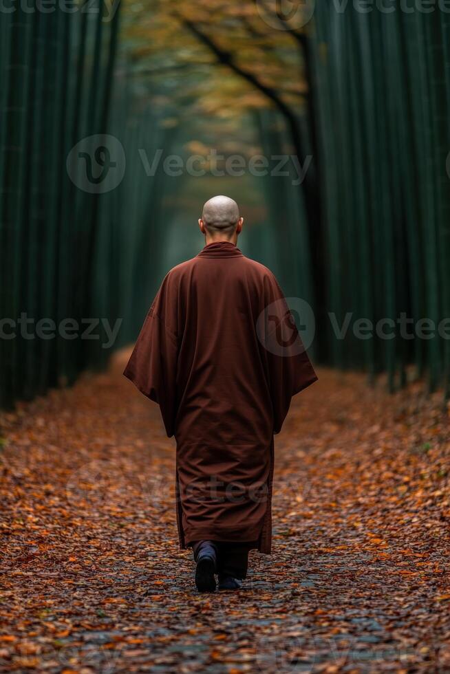 A monk walking through a serene forest path in autumn foliage photo