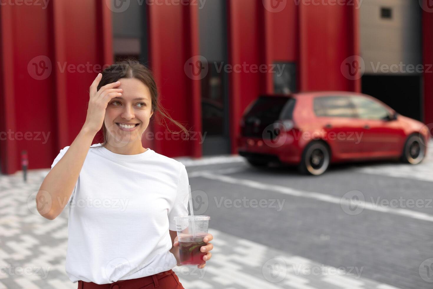 Attractive woman drinks fresh lemonade with red car on urban background photo