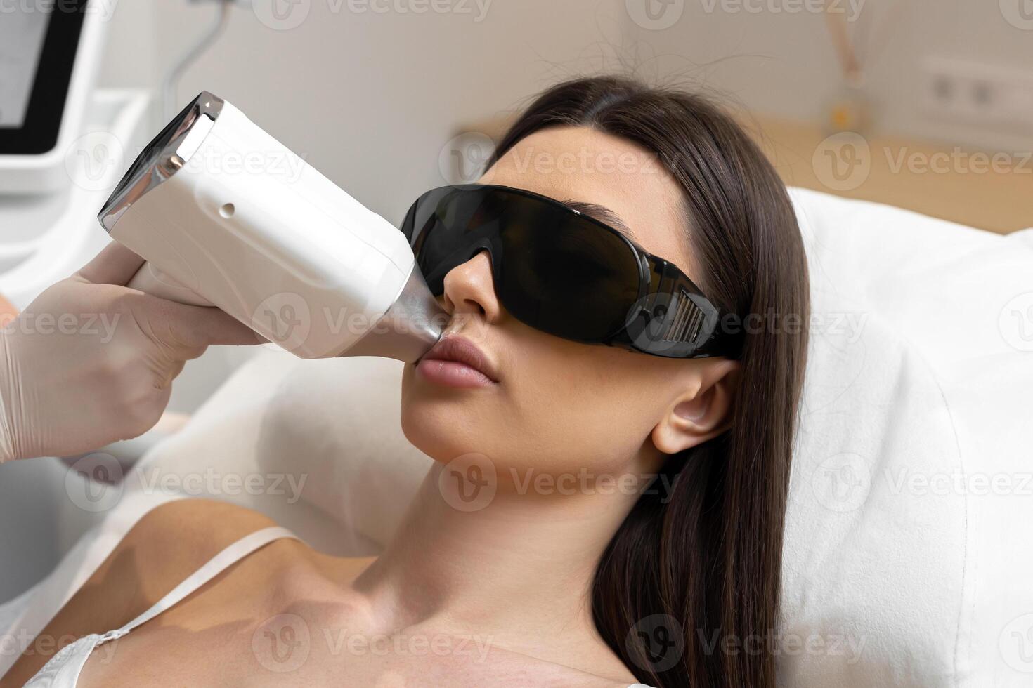 Cosmetologist make laser hair removal on woman's under nose photo