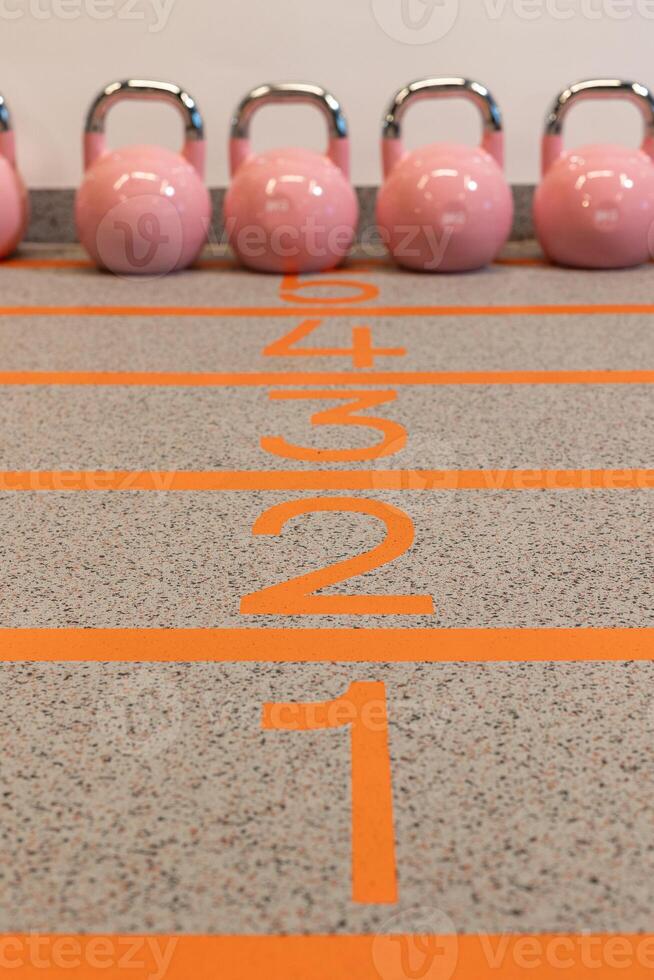 Pink kettlebells stand on a track with markings photo