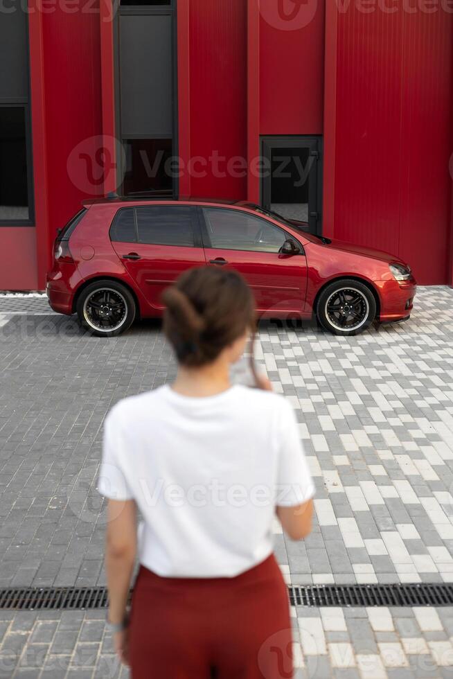 Attractive woman in stylish outfit standing in front of red car photo