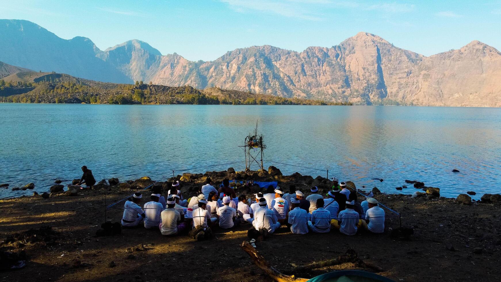Aerial from the summit of Rinjani shows the stunning Segara Anak Lake below, Surrounded by vibrant blue skies and clouds, the lake's serene beauty stands out against the dramatic landscape. photo